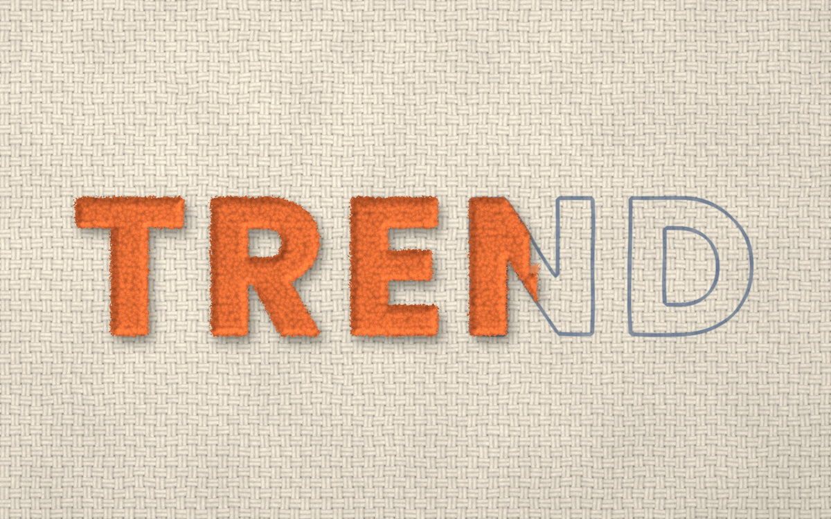 The word TREND tufted in orange yarn on tufting cloth, with the last letters still drawn in outline, waiting to be tufted