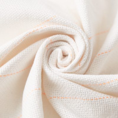 A close-up of a textured off-white woven fabric, Craftphilia tufting cloth , styled in a spiral swirl with thin orange dashed stitching details.
