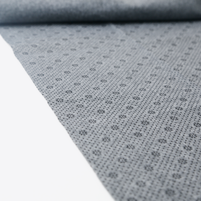 A craftphilia backing cloth close-up of a light gray fabric with a repeating small floral or starburst pattern, shown partially unrolled over a white surface.